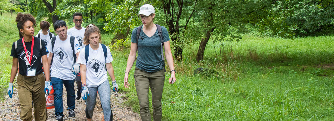 A professor leads a group of students on a walk through a park.