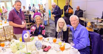 A table of four Golden Eagle alumni gather for a photo in front of a live band.
