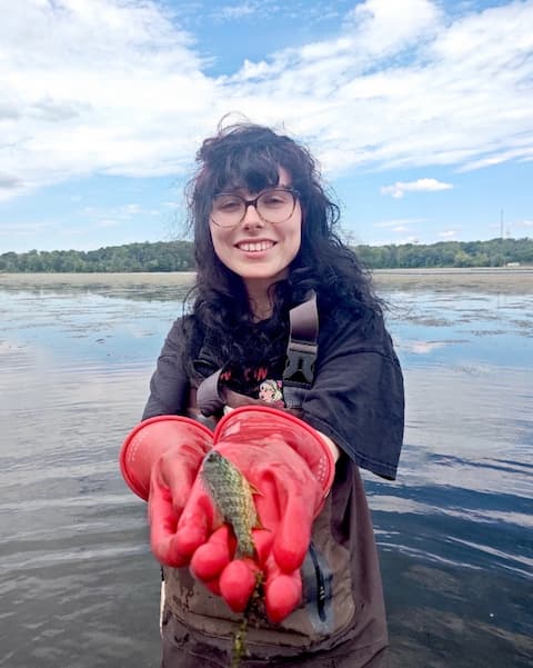 Summer Orledge doing river fieldwork and holding a fish.