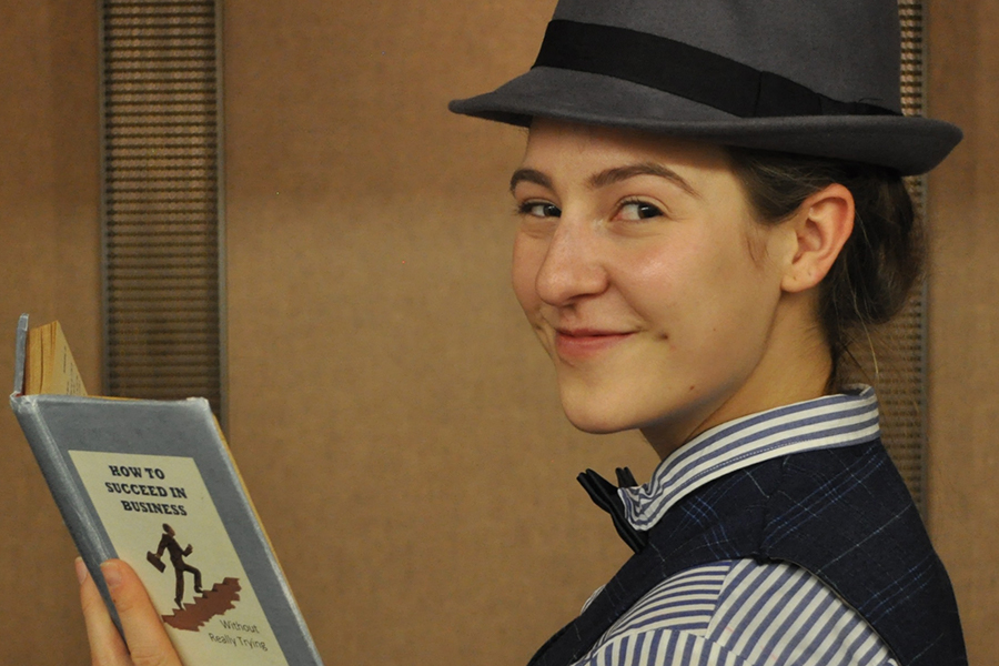 Woman in fedora holds book and raises an eyebrow.