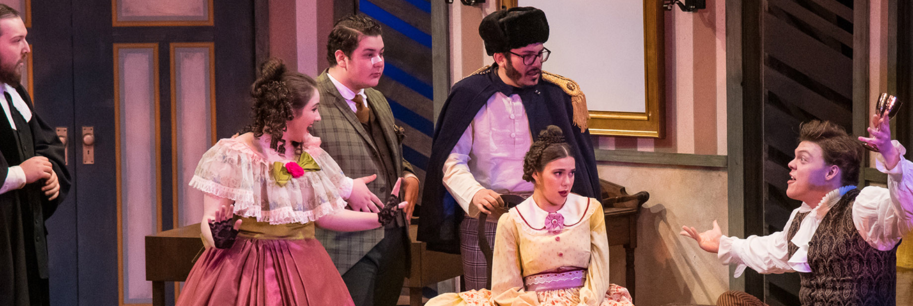 People in 1800s attire gather around a man who is wildly gesticulting