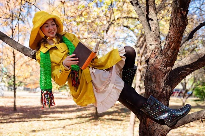 Sometimes the Rain cast member in a tree in rain gear with  book