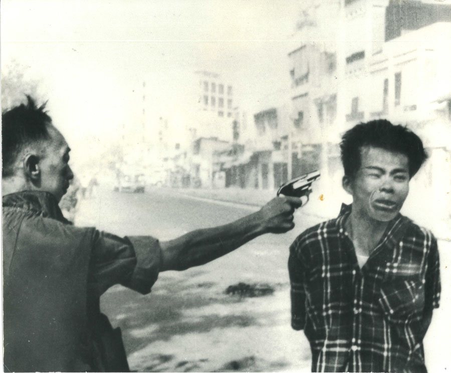 One man firing a gun point blank at the side of an agonized young man or boy's head. Nick Ut, photographer.