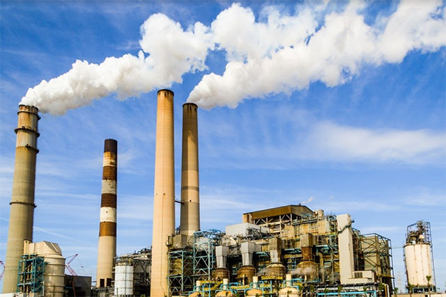Smoke pouring from multiple industrial stacks into blue sky.