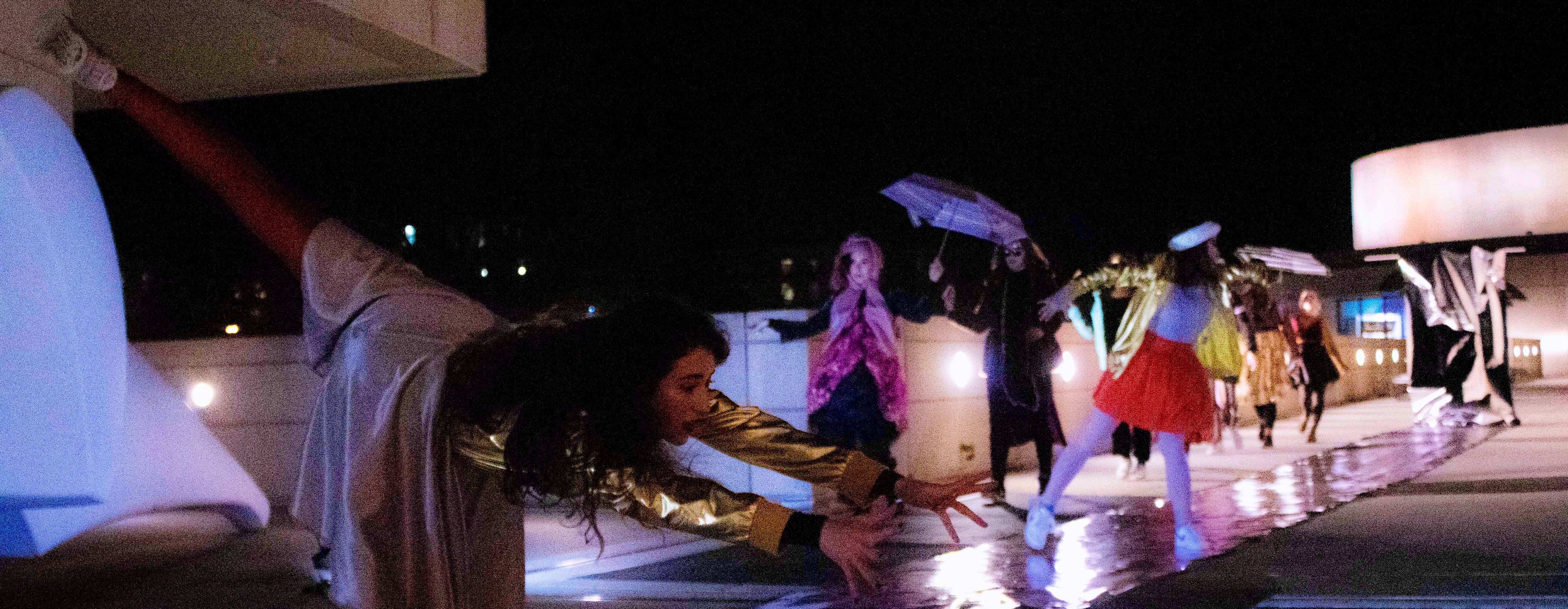 Dancers walk and dance an outdoor runway, holding objects like umbrellas