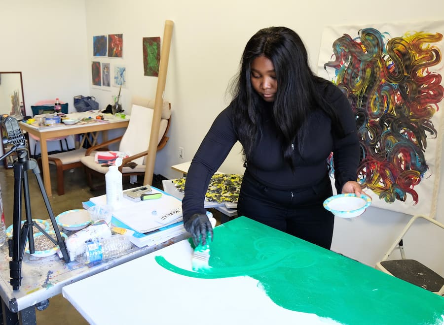 MFA student at work on a painting with other artwork in backgroud.