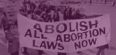Crowd marching with banner saying abolish all abortion laws now.