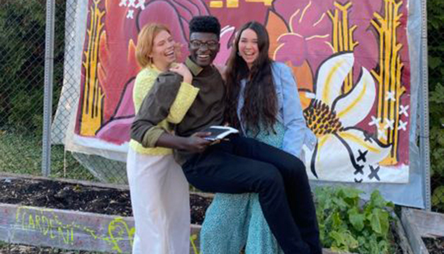 Sydney Spencer (’22) and Ashley Hocking (’24) holding artist TreVaughn Ellis (’24) in front of the garden mural