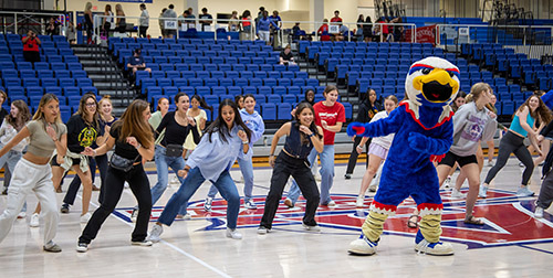 Clawed the eagle and students dancing on a basketball court