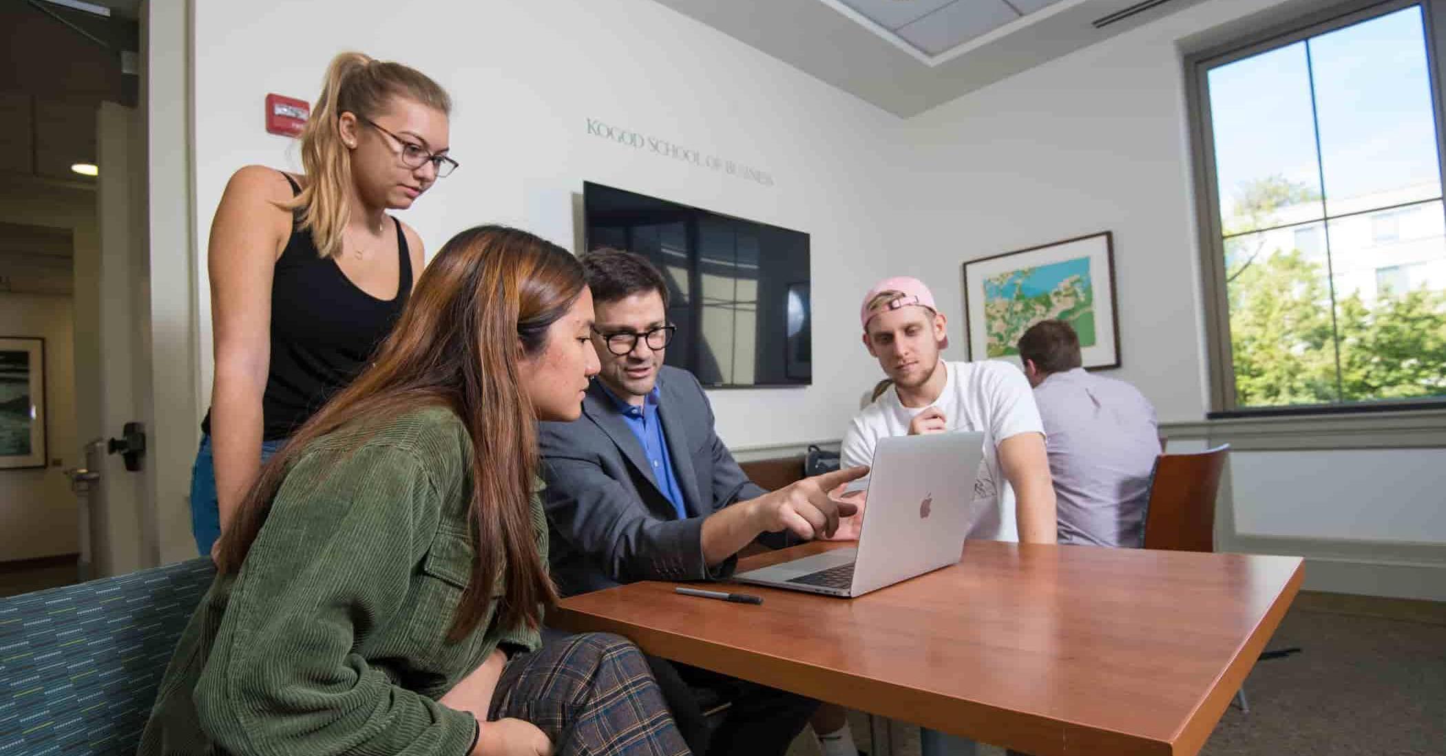 Group of students with a professor looking at a laptop