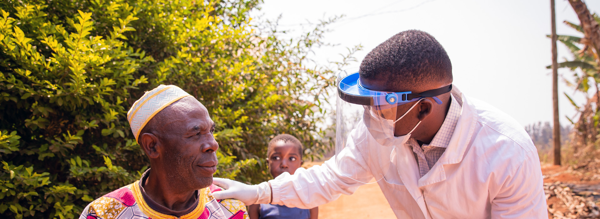 An African doctor helps an elderly African man. A child stands behind them as they talk.