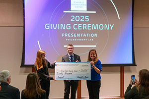 Two students in the Philanthropy Lab class present Briya's executive director, Christie McKay, with a check