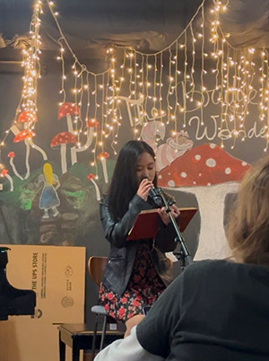 Ruchel Limbos sits on a stool at a microphone reading from an open mic in front of an audience