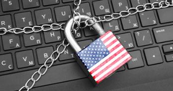 A padlock with an American flag painted on it is chained over a laptop
