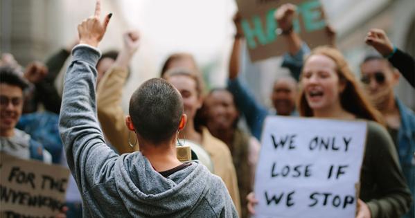 young girl's back with her hand pointing to the sky as she faces a crowd of young protests