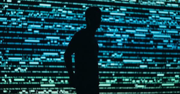 Silhouette of a person stands in front of a wall with text code displayed