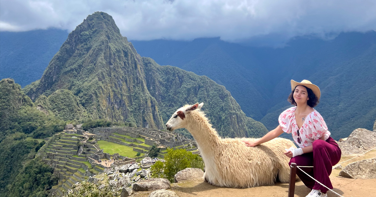 A student poses with a llama in front of Machu Picchu.
