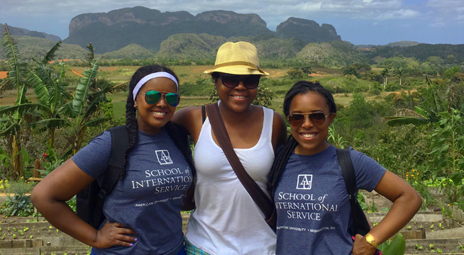 Three students studying abroad stand in front of lush vegetation.