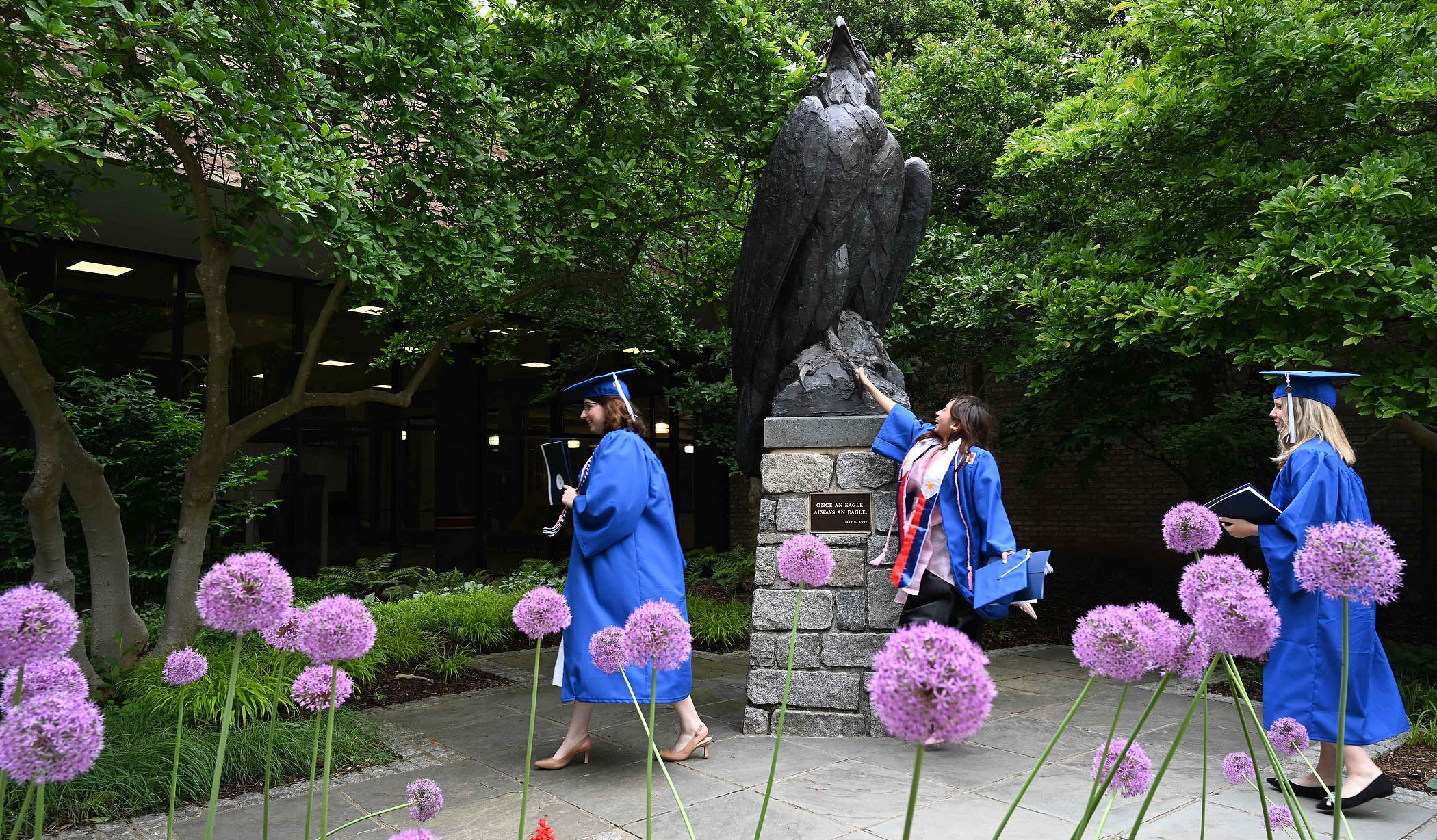 Graduates in commencement regalia touch the AU eagle statue outside Bender Arena.