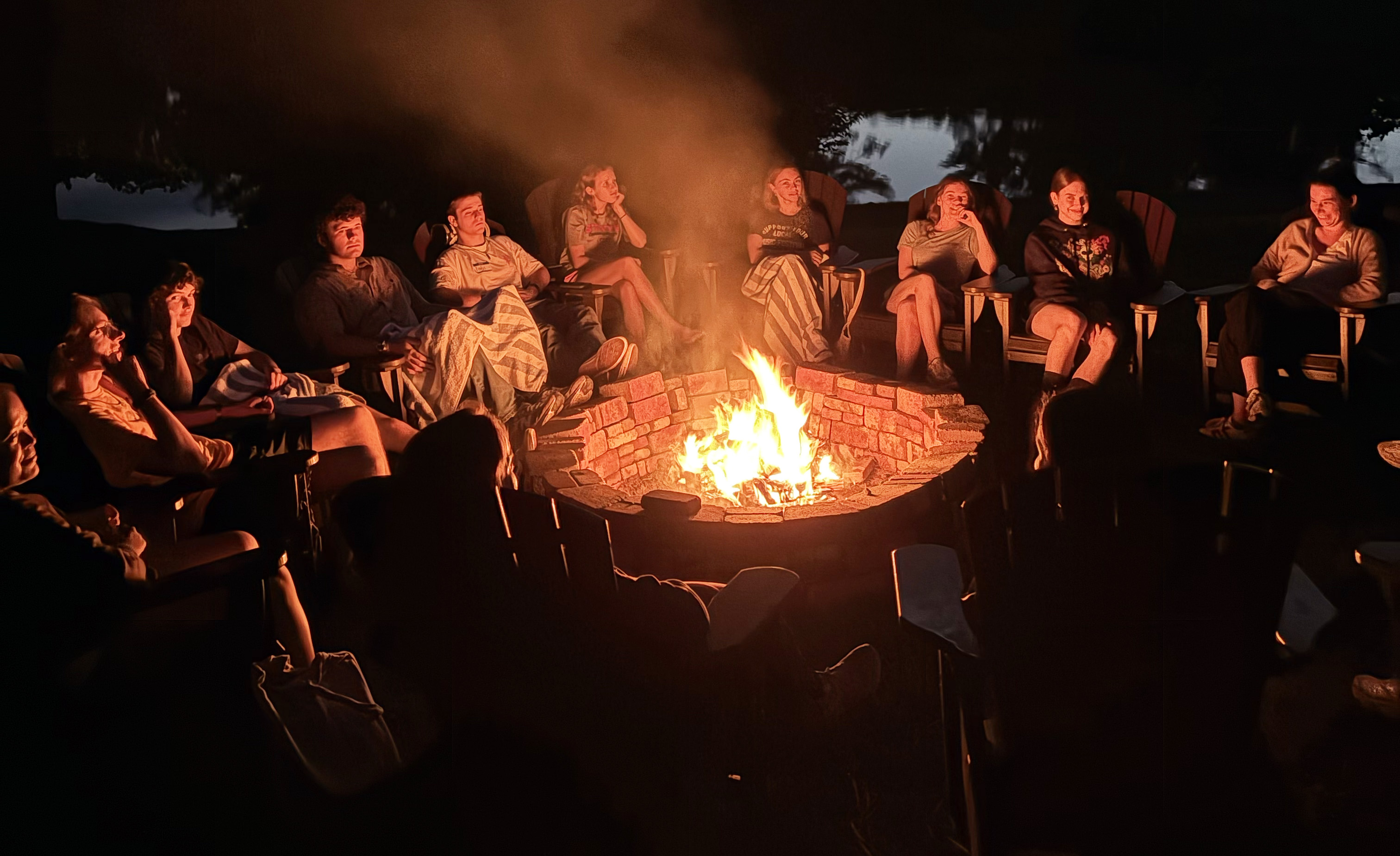 Smiling Earth Scholars sit in the dark woods around a campfire.