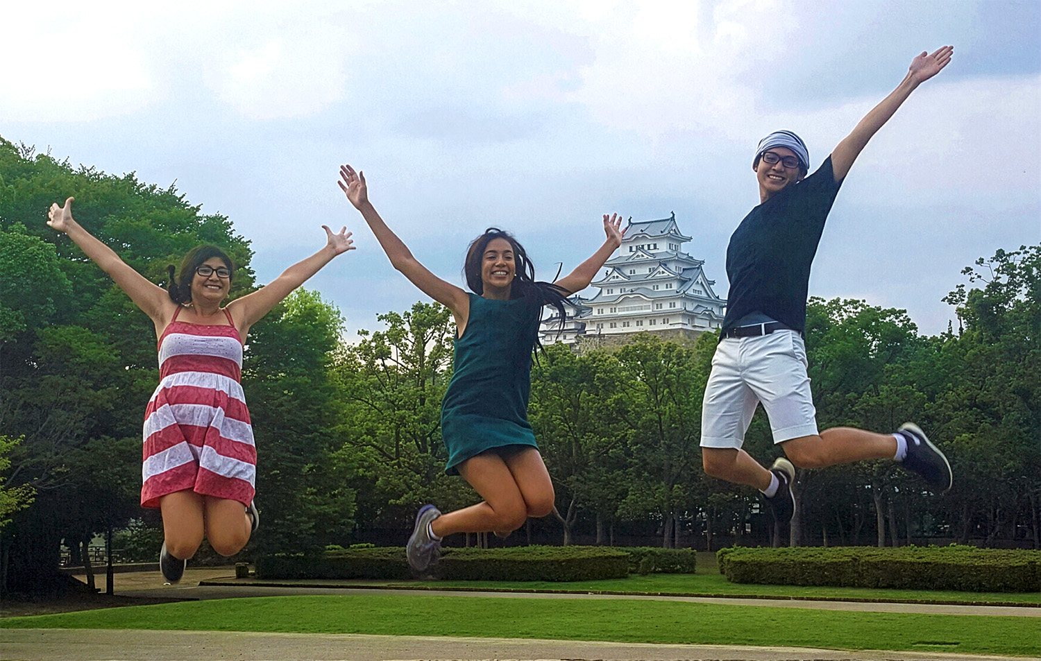 Three students jump for a pose in front of a historic building in Japan.