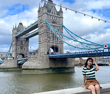 A student sits on a wall in front of the London Bridge.
