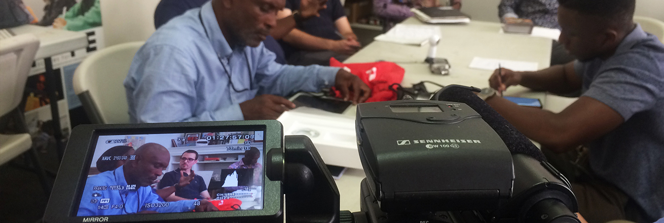 Some men being filmed sitting around a table and talking