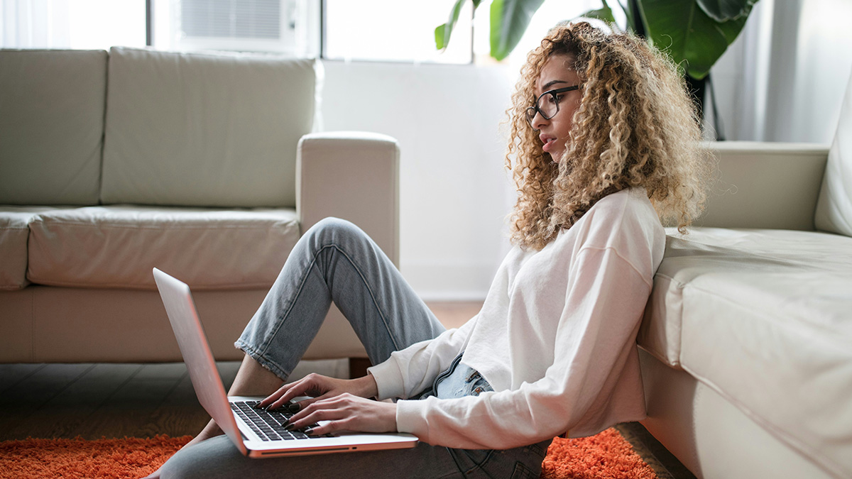 A student works at home leaning on a couch.
