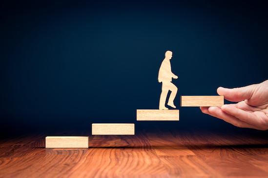 Wooden figure walking up wooden stairs on dark blue background to illustrate moving upward and coaching