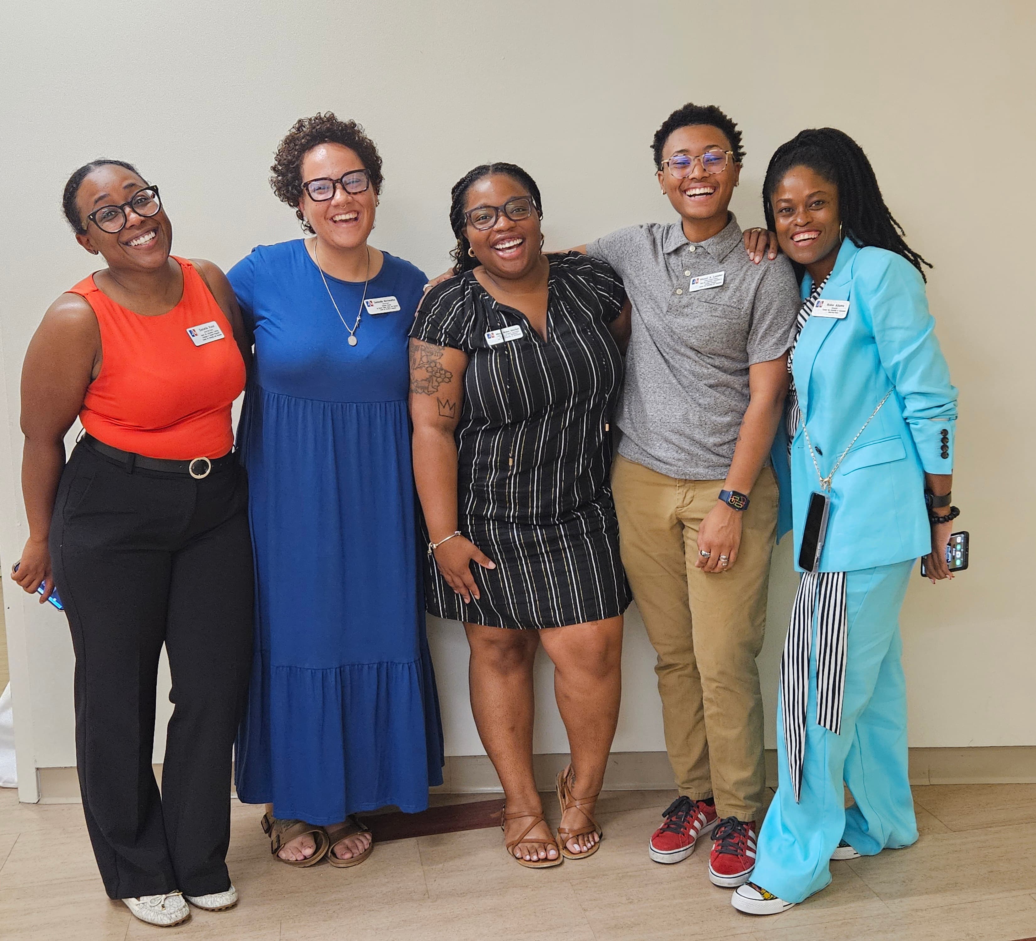 Five staff members from the Center for Student Belonging stand in front of a beige wall and smile at the camera.