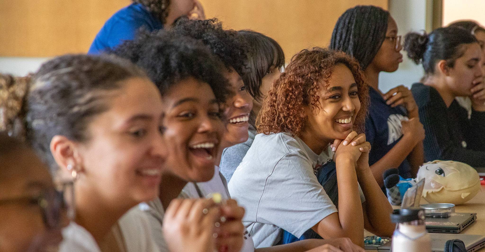 Students smile and laugh sitting at a table in a lecture hall.