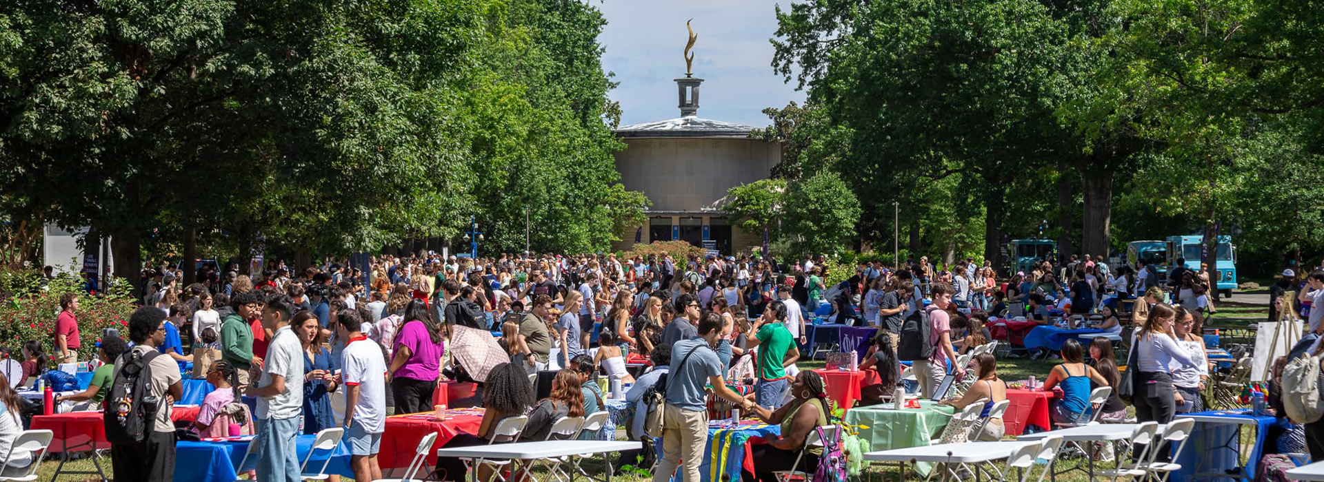 A crowd of students is on the Quad for the Student Involvement Fair. Students on either side of tables for different organizations, talking to each other.