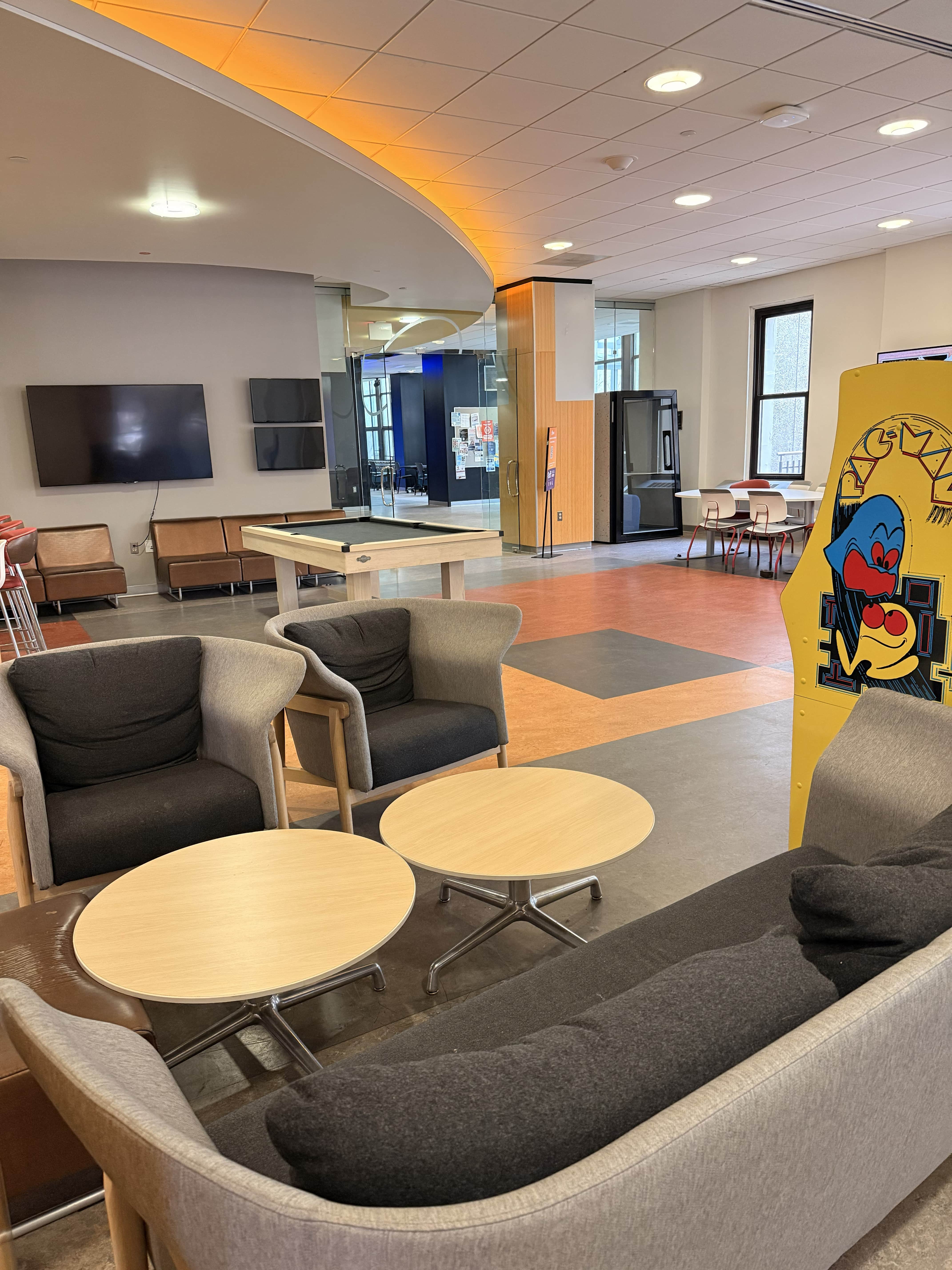 A photo of the game zone on the first floor of Mary Graydon Student Center. A couch and chairs in the foreground are surrounded by a pool table and a Pac-Man arcade cabinet.