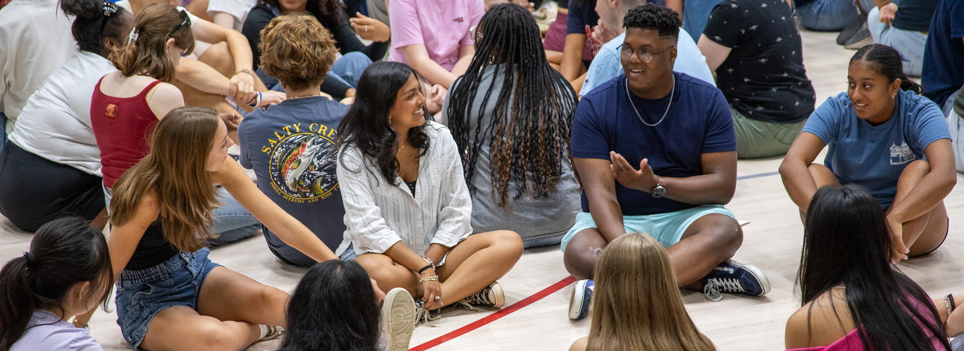 A group of students sit on the floor of Bender Arena, chatting.