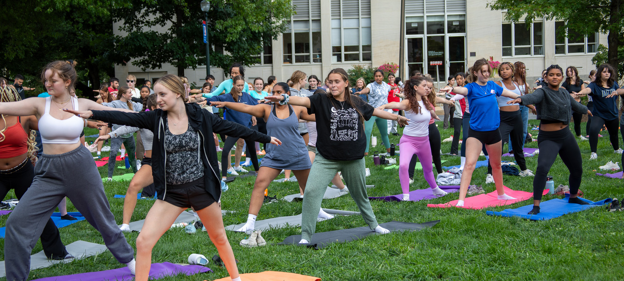 Students stretch out their arms in an outdoor yoga class.